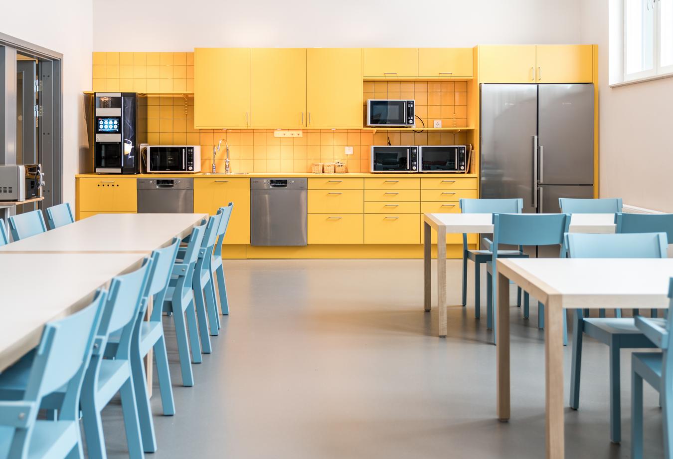 Canteen with yellow kitchen and light blue chairs. Photo