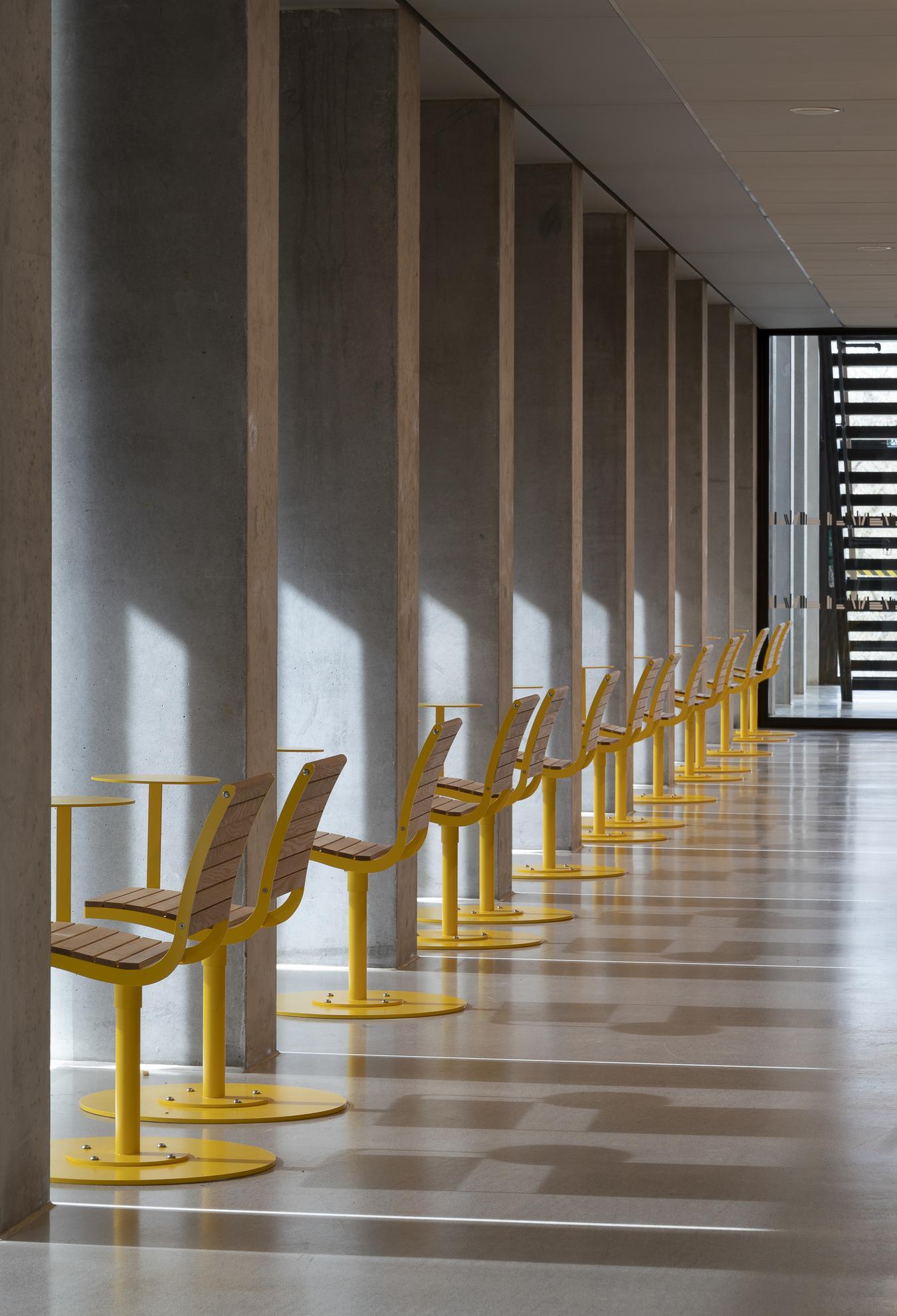 Hall med betongpelare och gula stolar. Foto
